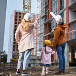 A back view of a man, woman and child wearing safety helmets, observing a construction site, emphasising workplace safety and teamwork in the construction industry